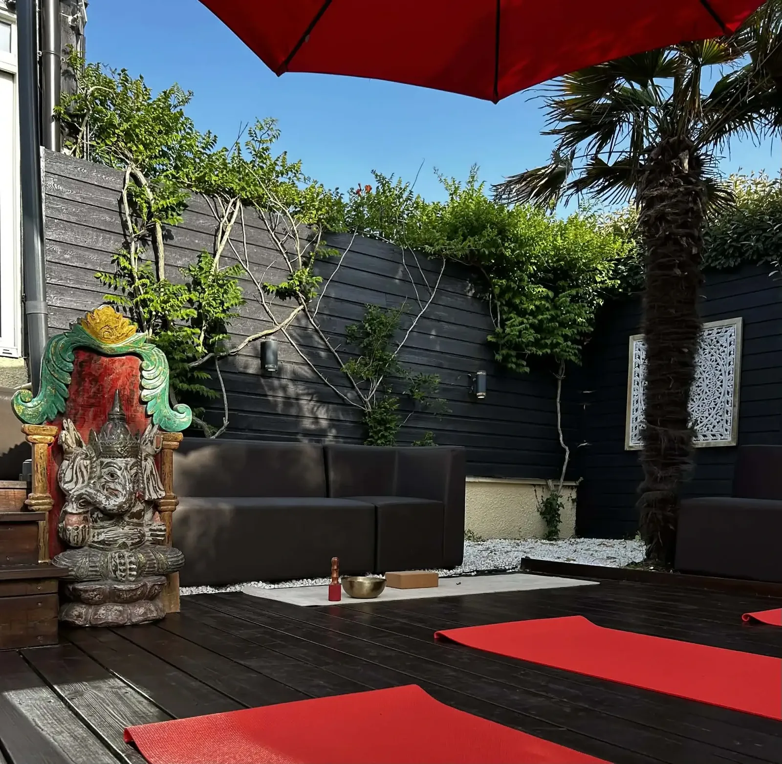 Ambiance zen de la terrasse à Moliets : parasol rouge, statue Ganesh, canapés